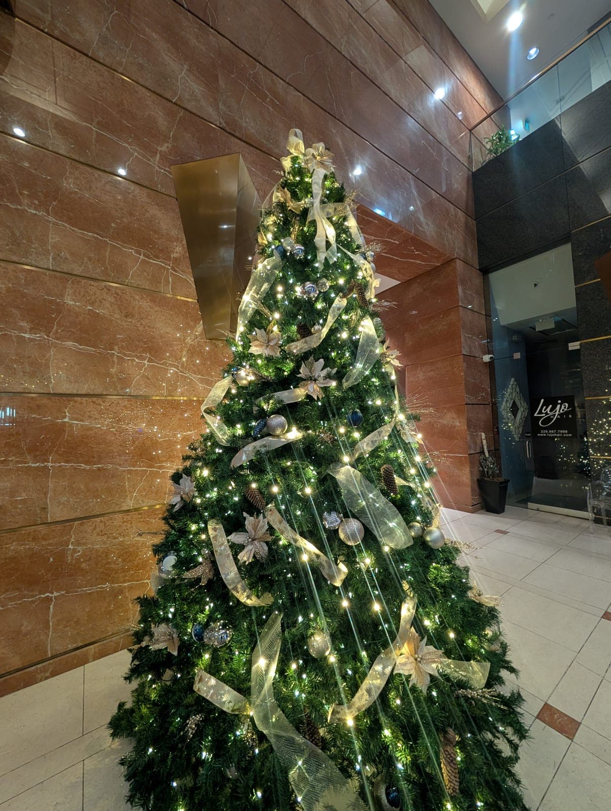 Upward view of a decorated Christmas tree with gold ribbon and ornaments in an upscale corporate lobby.