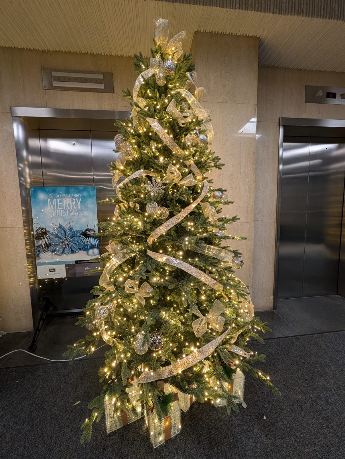 Warm-white Christmas tree with gold ribbon by elevators in a commercial building lobby