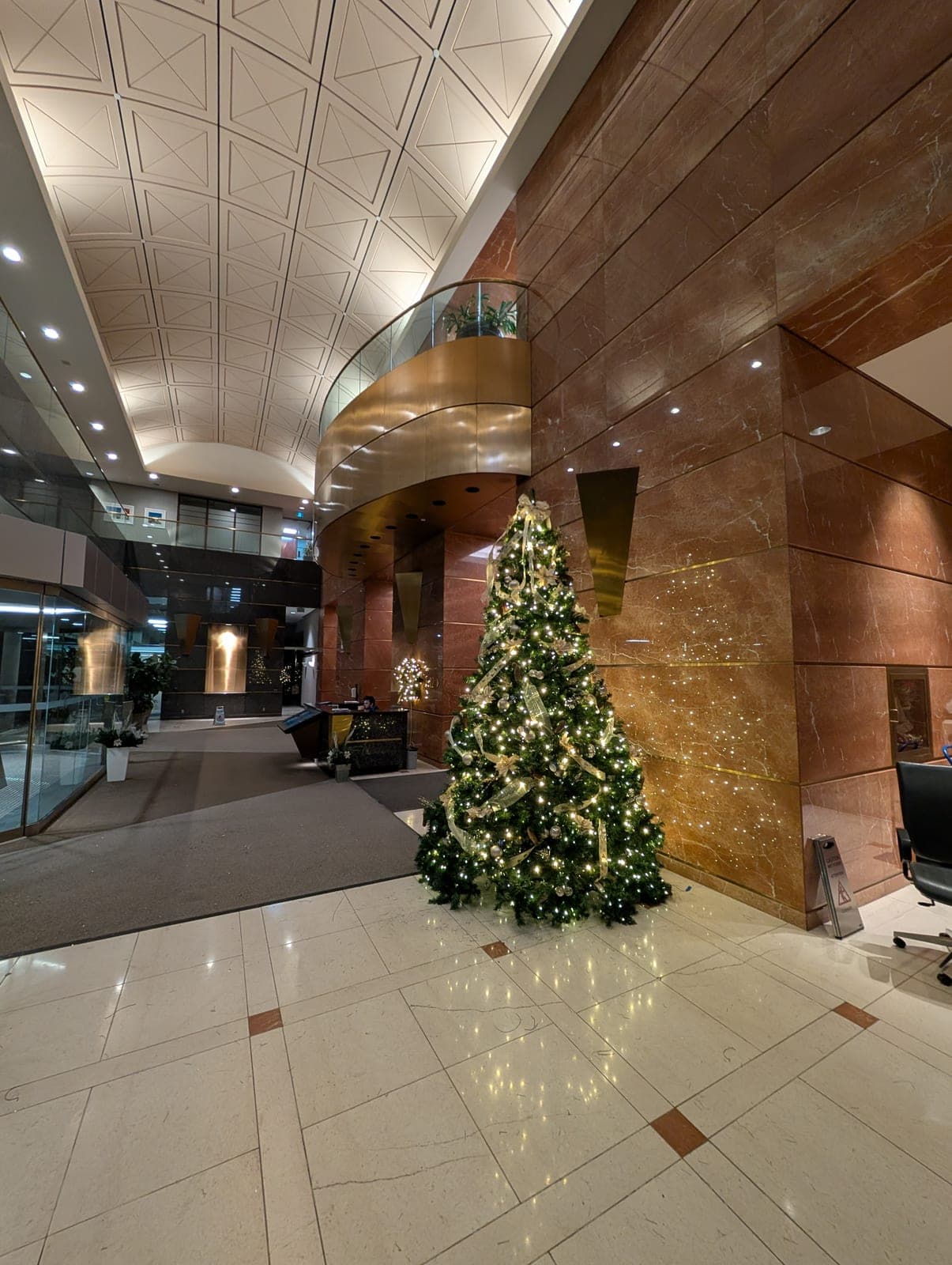 Tall decorated Christmas tree in a grand corporate marble atrium lobby with warm-white lights