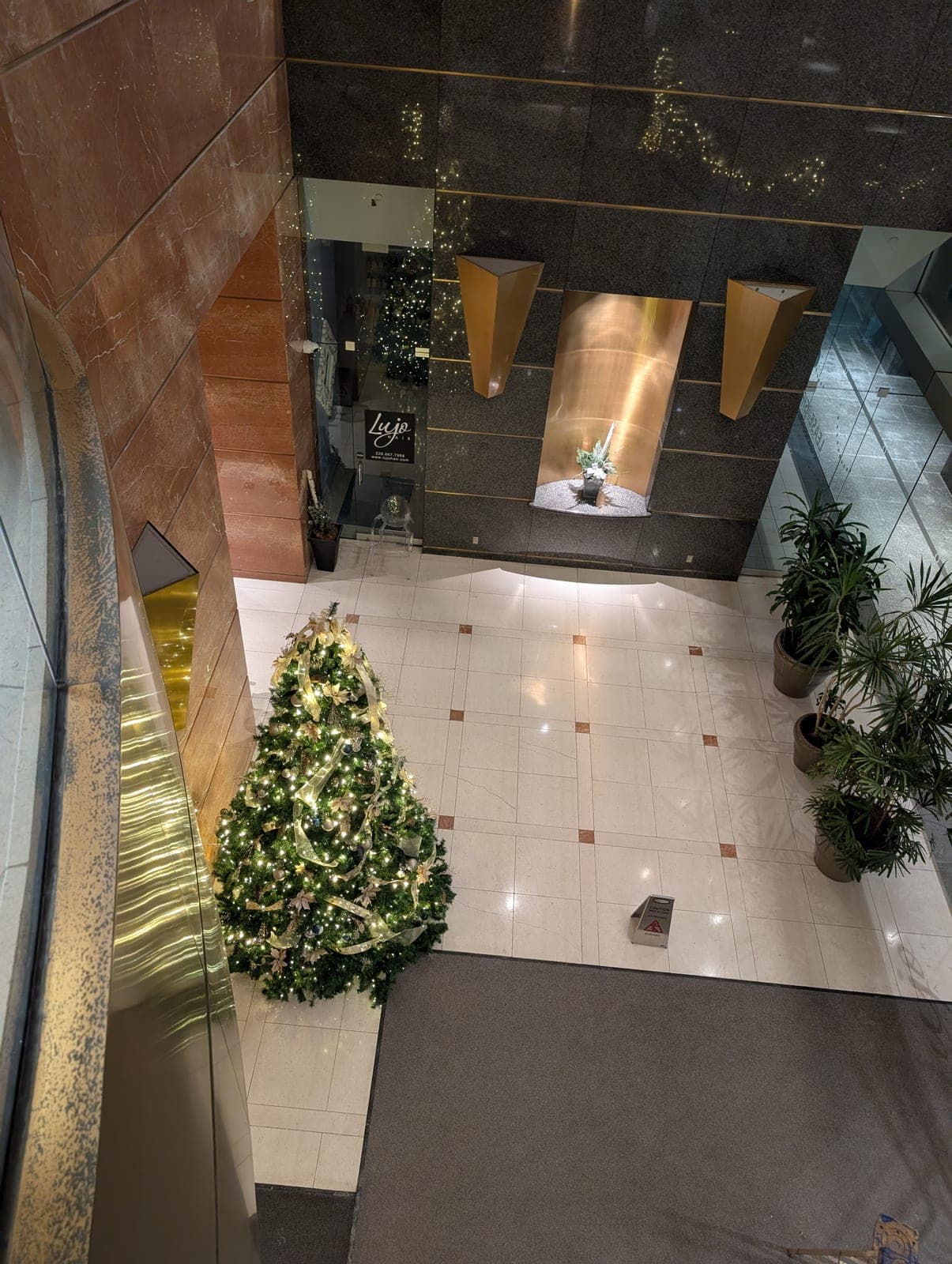 Decorated Christmas tree in a polished marble office lobby with potted palms and warm accent lighting.