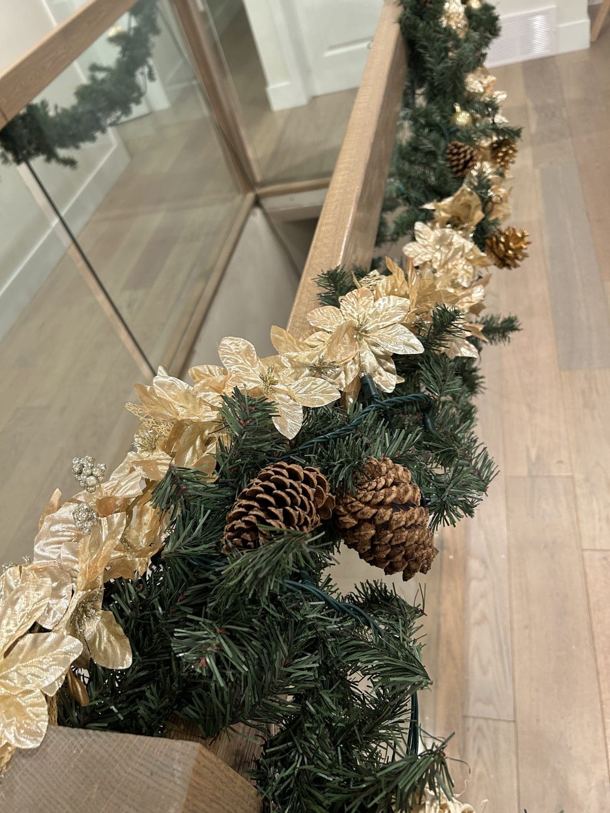 Gold poinsettia and pinecone Christmas garland wrapped along an indoor wood staircase railing