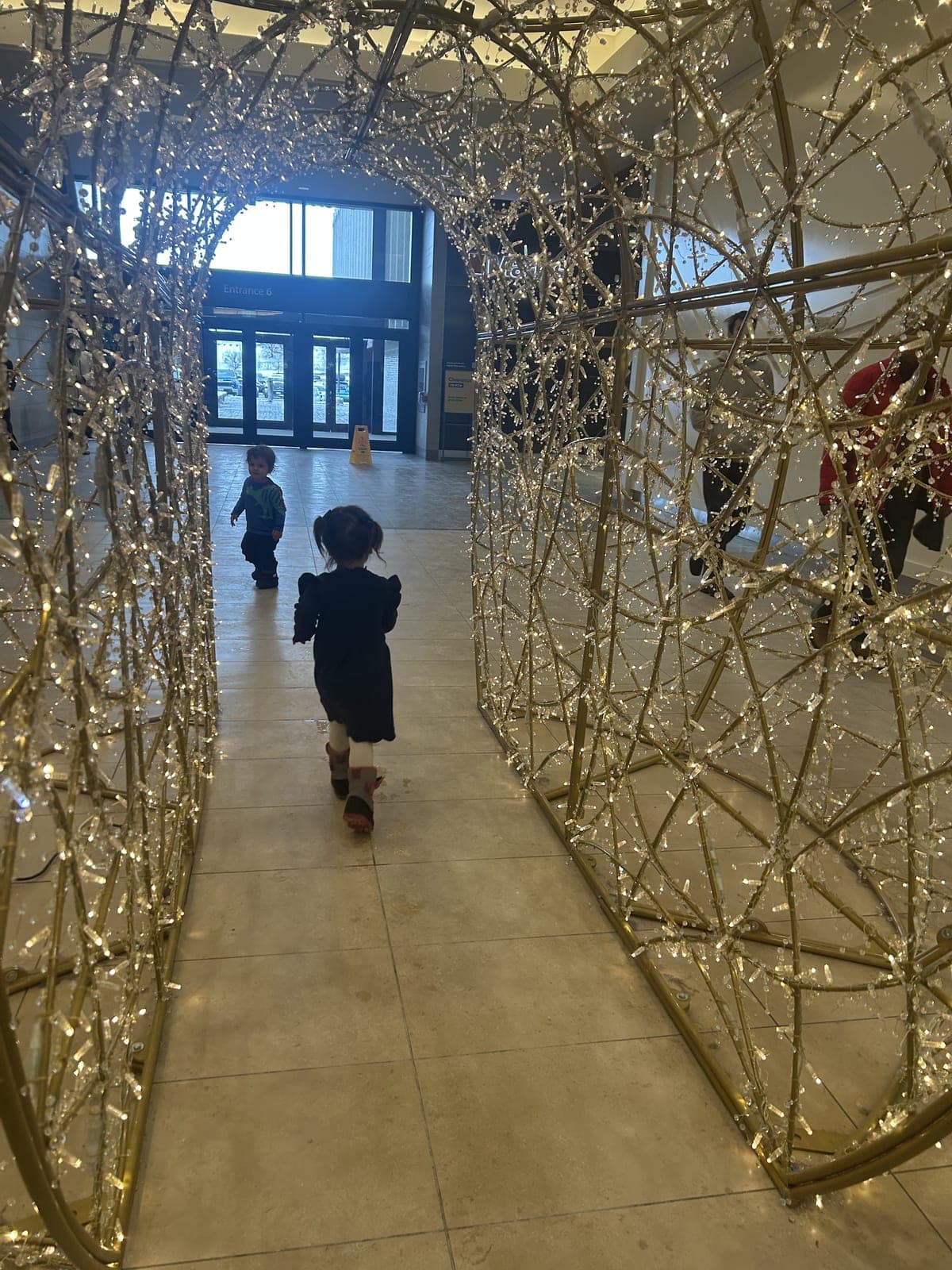 Illuminated gold Christmas light archway tunnel in a building lobby with visitors walking through.
