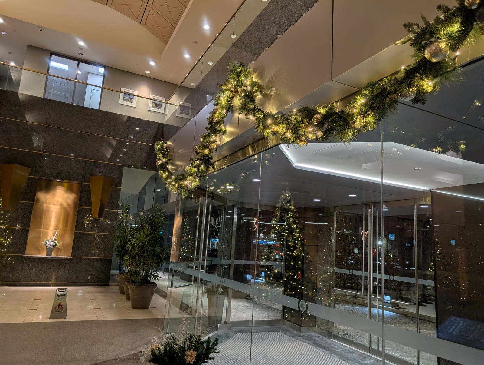 Lit evergreen garland arching over the glass entrance doors of an upscale office lobby at night.