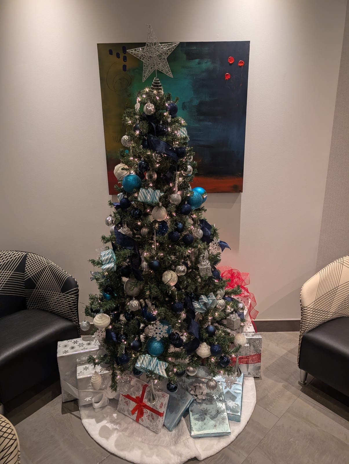 Navy and silver decorated Christmas tree with wrapped gifts in a modern business lobby