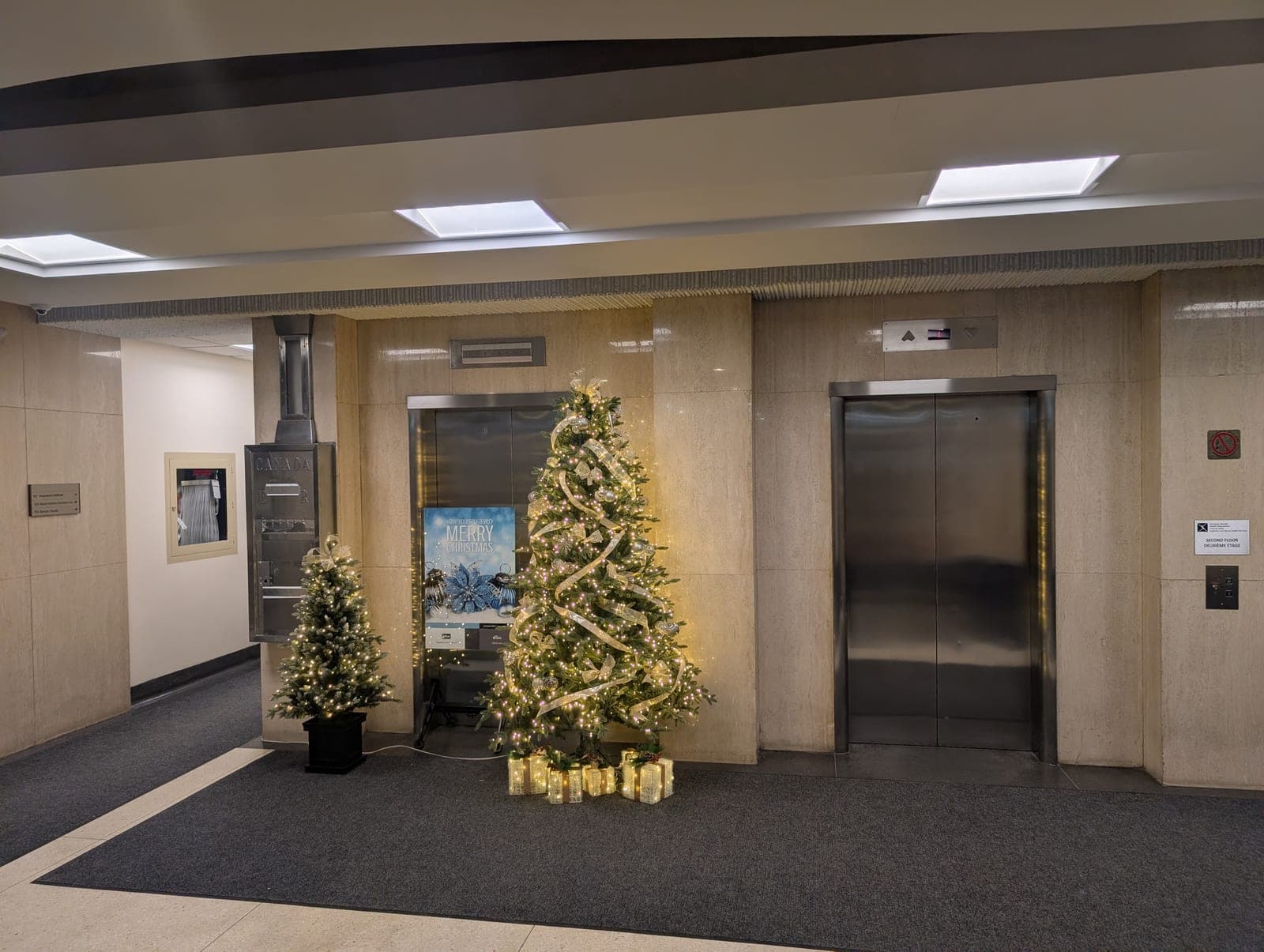 Elegant Christmas tree with gold ribbon and lit gifts in a marble office elevator lobby