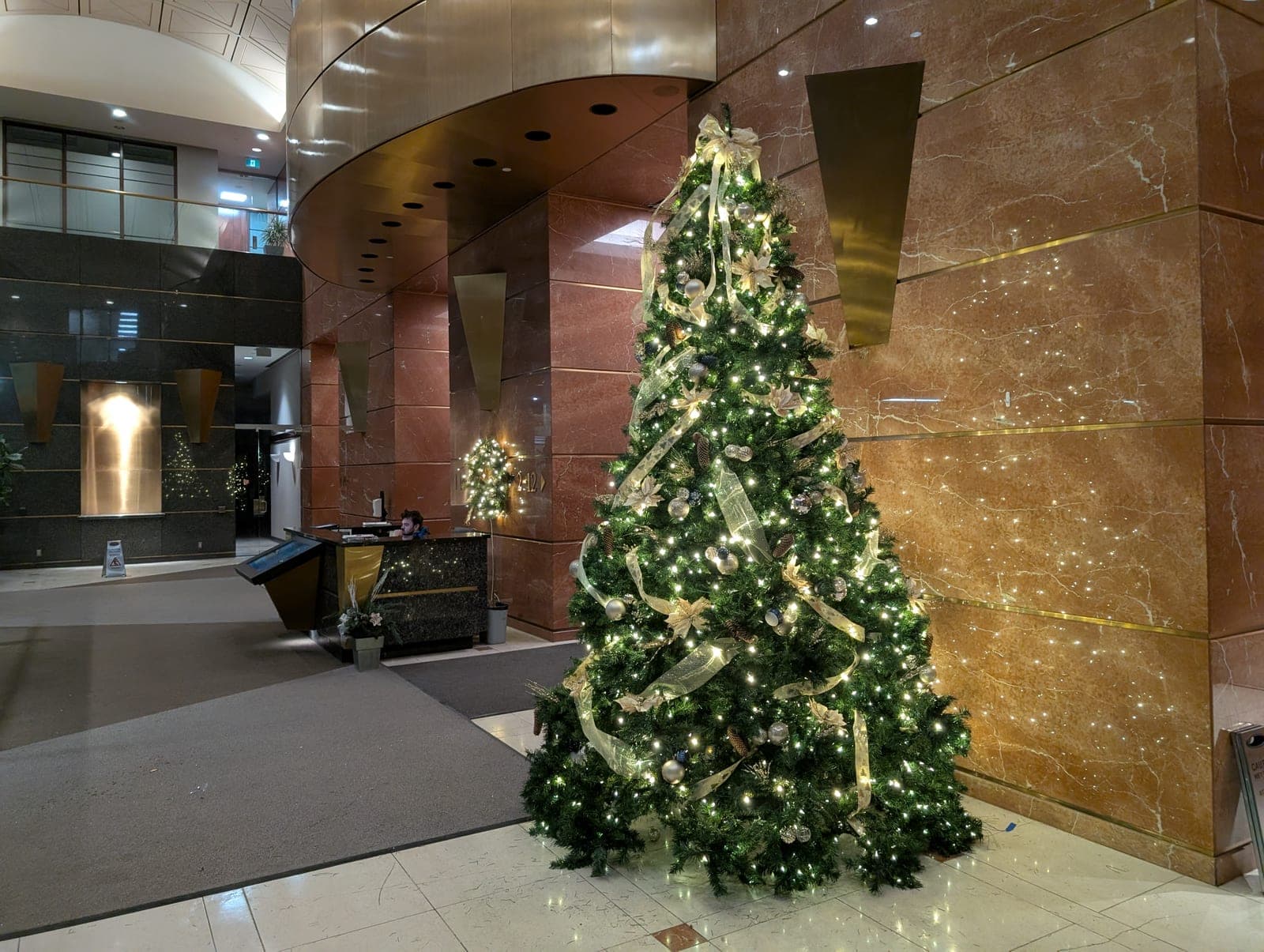 Decorated Christmas tree lighting up a marble office tower lobby entrance.